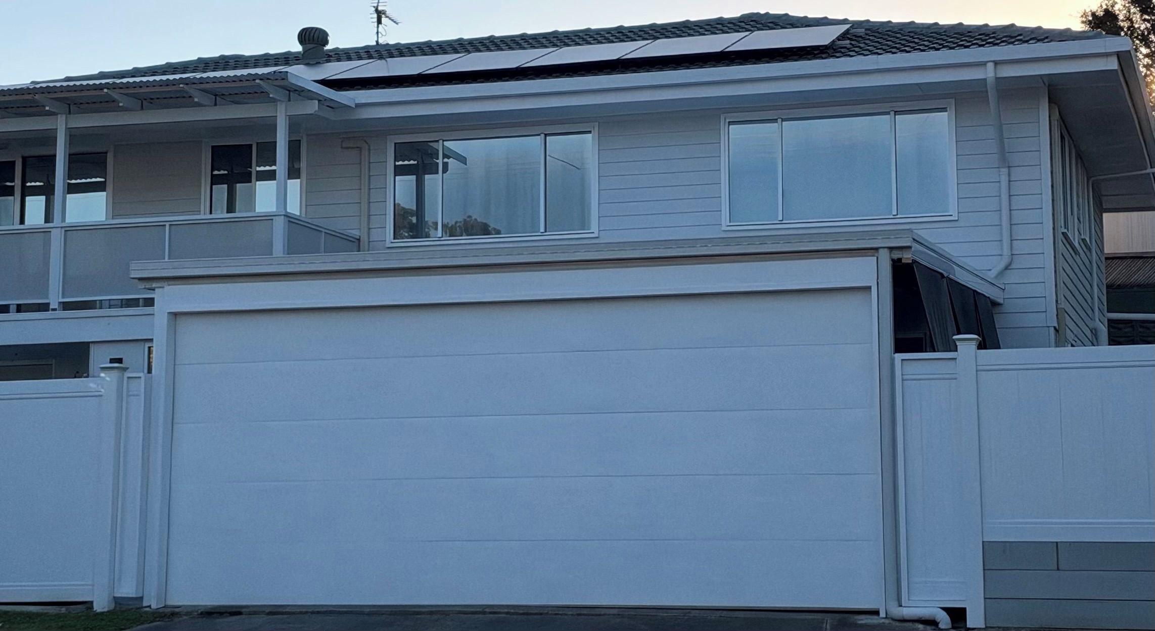 A two-story house with a garage, large windows, and a solar panel array on the roof.