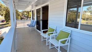 A covered porch with two white chairs and a bench, a sliding glass door, and a view of the street. - Holiday House Southport near Surfers Paradise. (Southport)