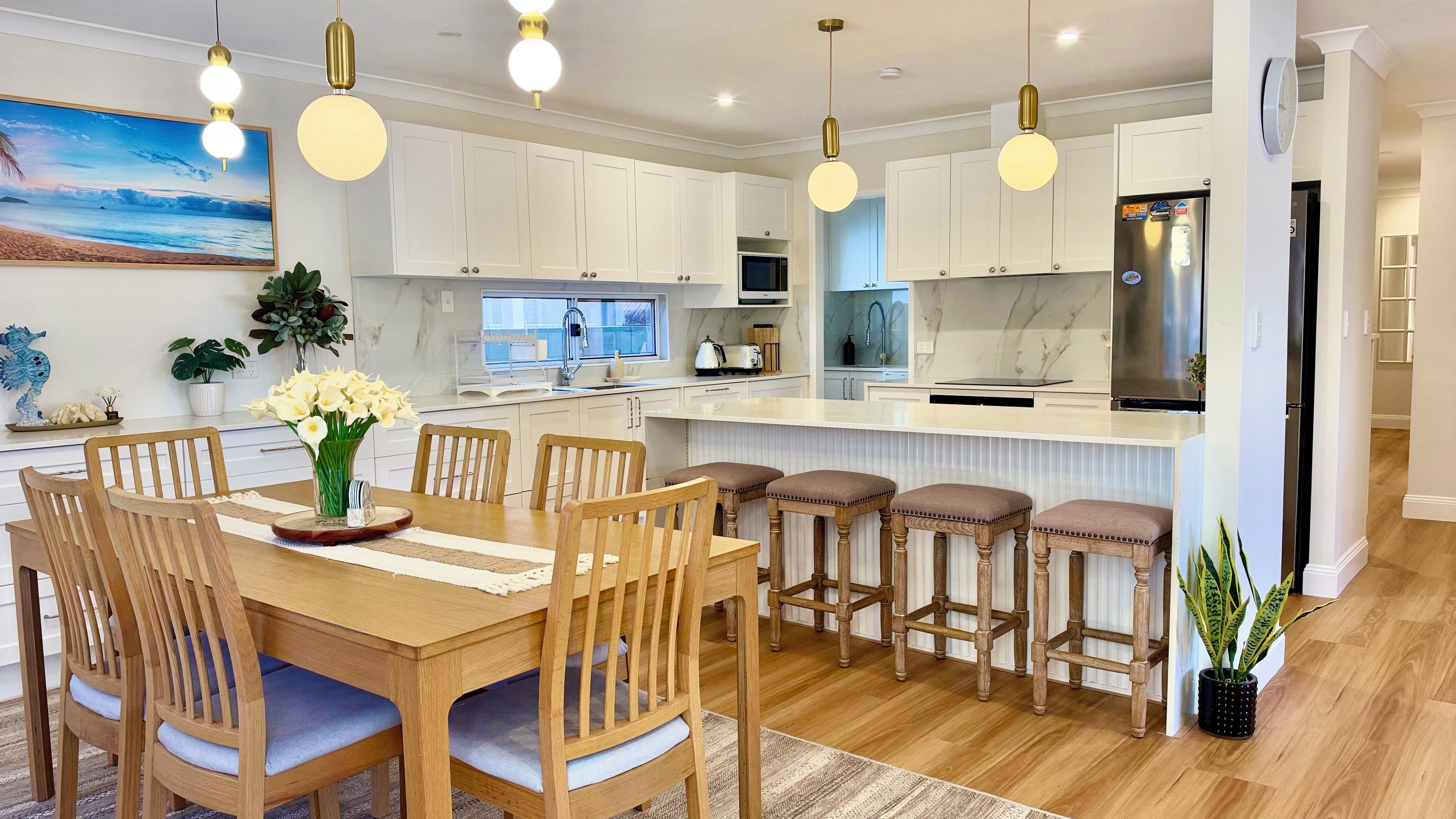 A modern kitchen with white cabinets, a central island, bar stools, and pendant lighting.
