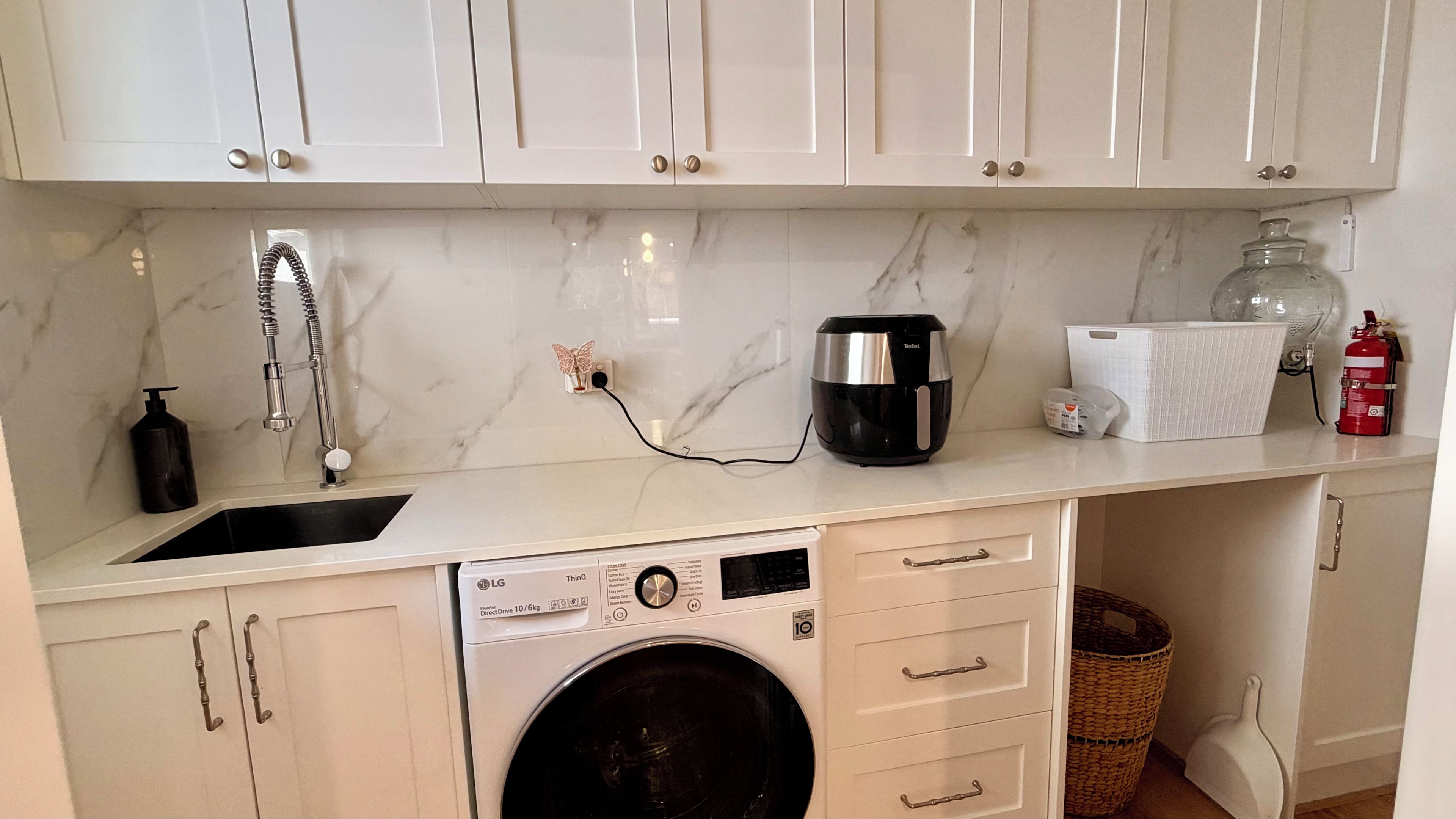 A compact kitchen with a washing machine, a coffee maker, and a fire extinguisher.