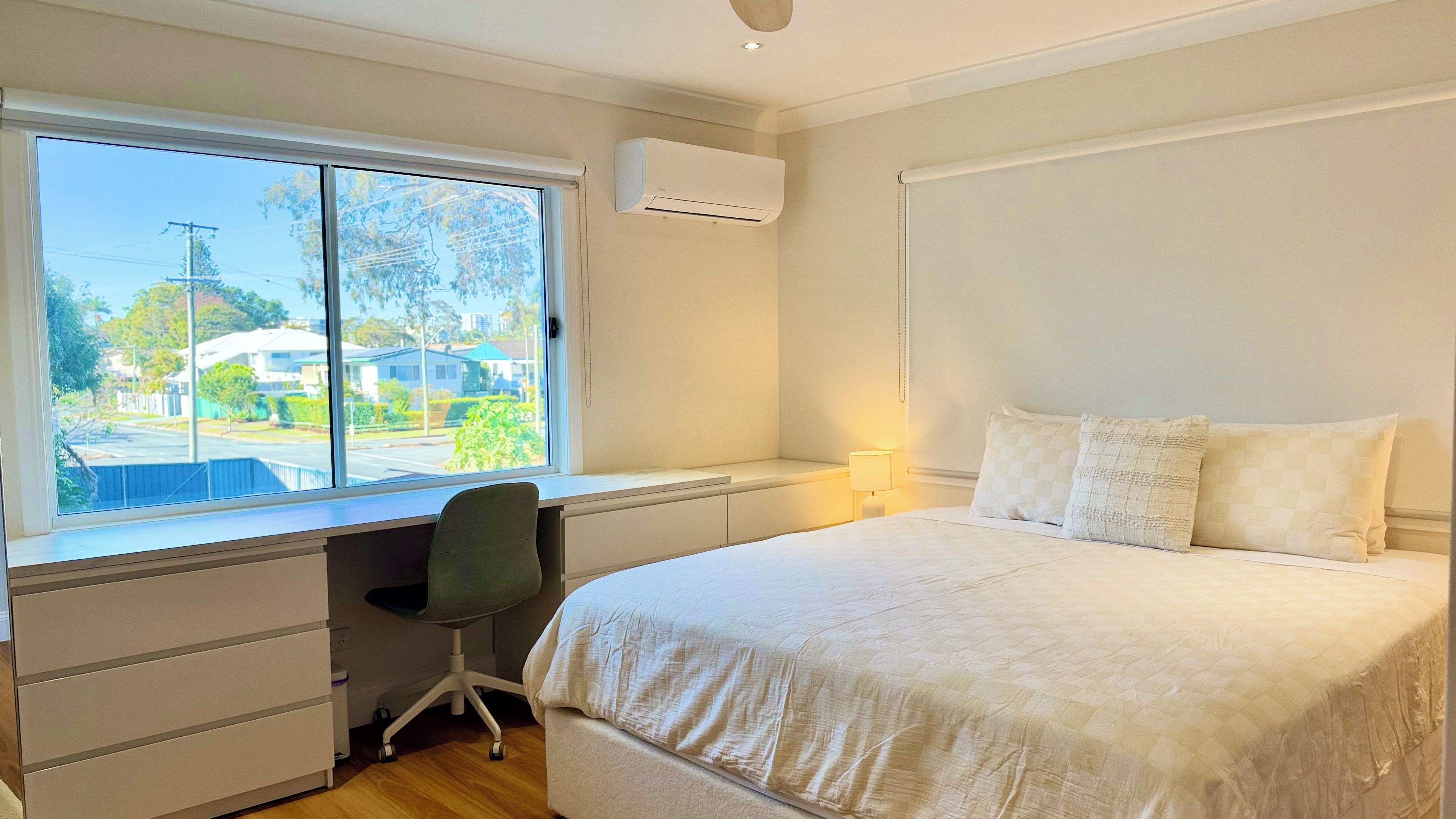 A bedroom with a large bed, a desk, and a window overlooking a street.