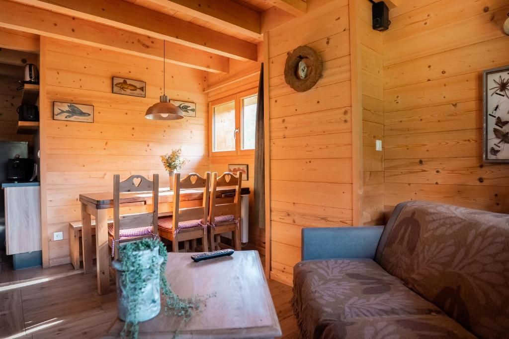 Interior de una cabaña de madera con comedor, sofá y una pequeña mesa con una planta.