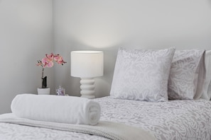 Een net opgemaakt bed met een beddekleed met een patroon, een wit kussen en een opgerolde witte handdoek.