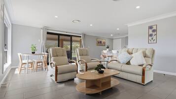 A modern living room with a sofa, two armchairs, a coffee table, and a dining area with a table and chairs.