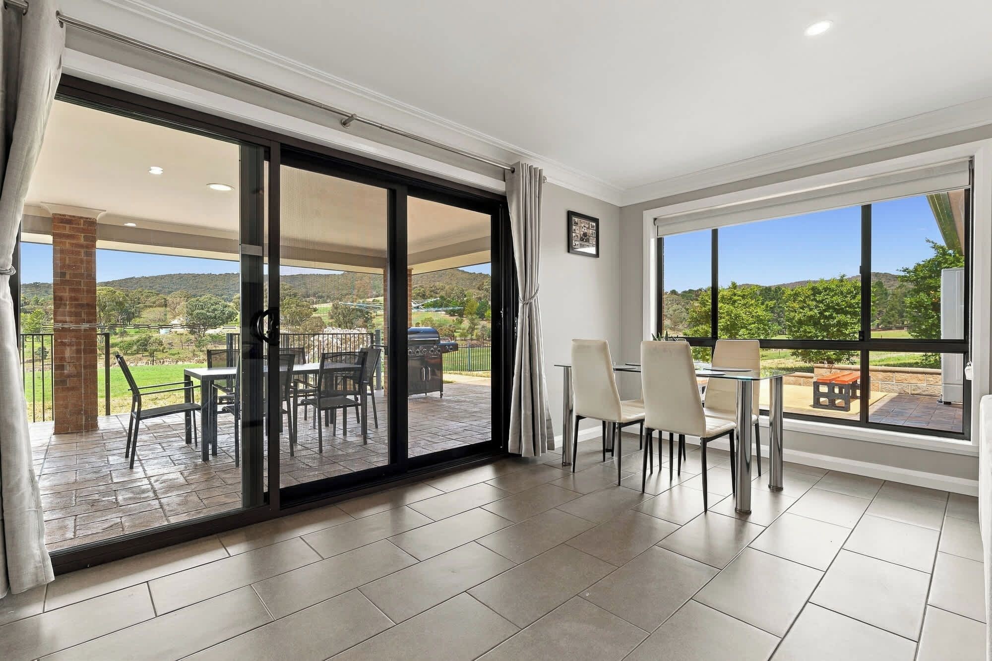A spacious room with a sliding glass door leading to an outdoor patio, a dining area with chairs and a table, and a large window offering a view of the outdoors.