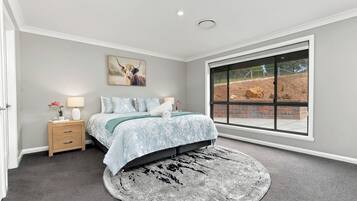 Un dormitorio con un ventanal grande, una cama con ropa de cama floral, una mesita de noche y una alfombra.