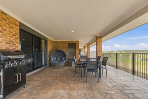 Een overdekt terras met een barbecue, zitplaatsen en uitzicht op het platteland.