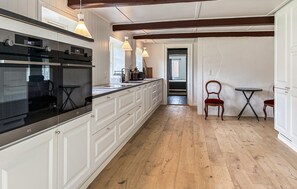 A kitchen with white cabinetry, a black oven, and a wooden floor. There are pendant lights above the counter and a small table with chairs. - Gorgeous home in Skærbæk with WiFi (Skærbæk)