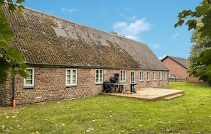 Un bâtiment en briques avec un toit en pente, une terrasse en bois et une cour gazonnée.