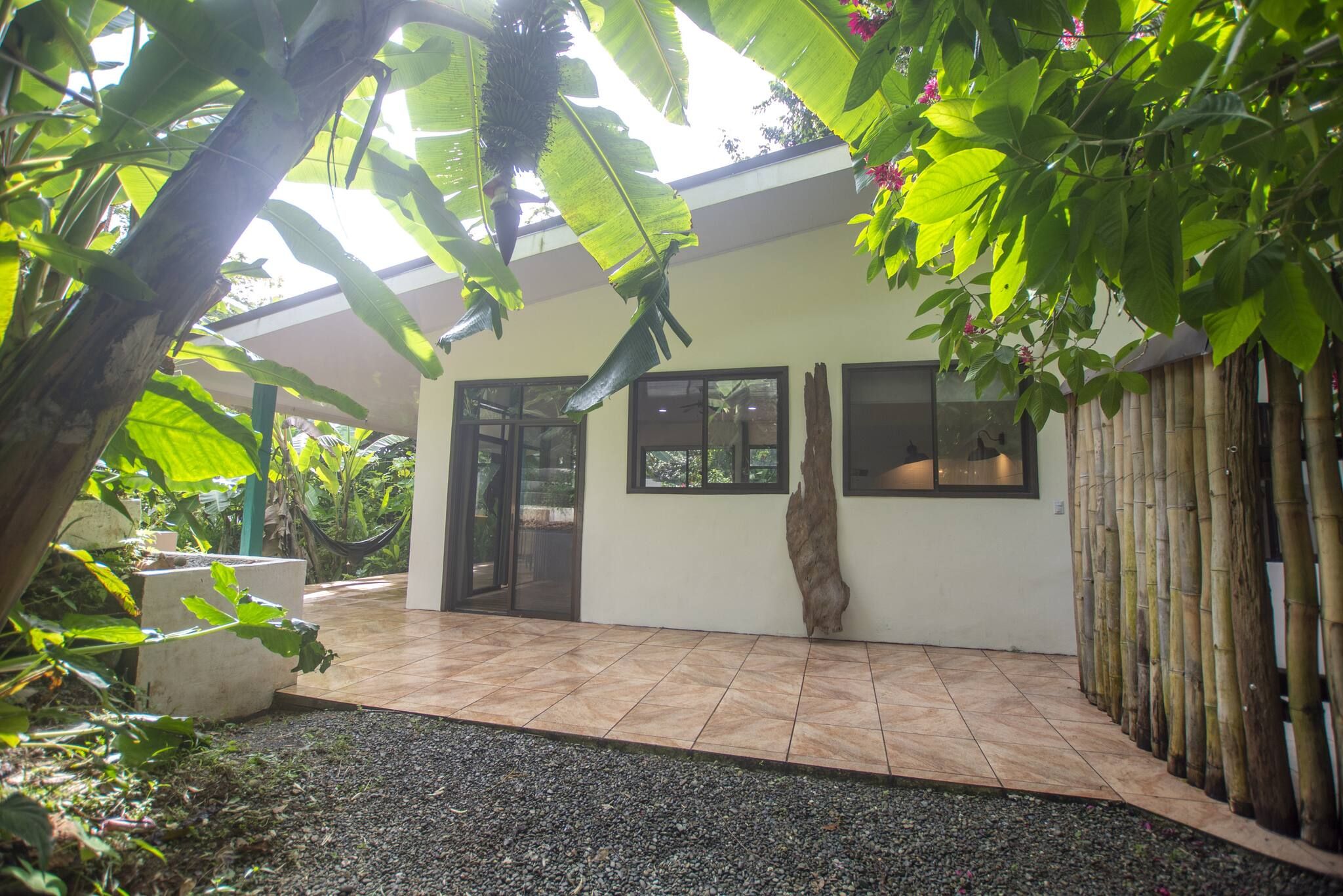 A covered patio area with a tiled floor, a large window, and a bamboo fence.