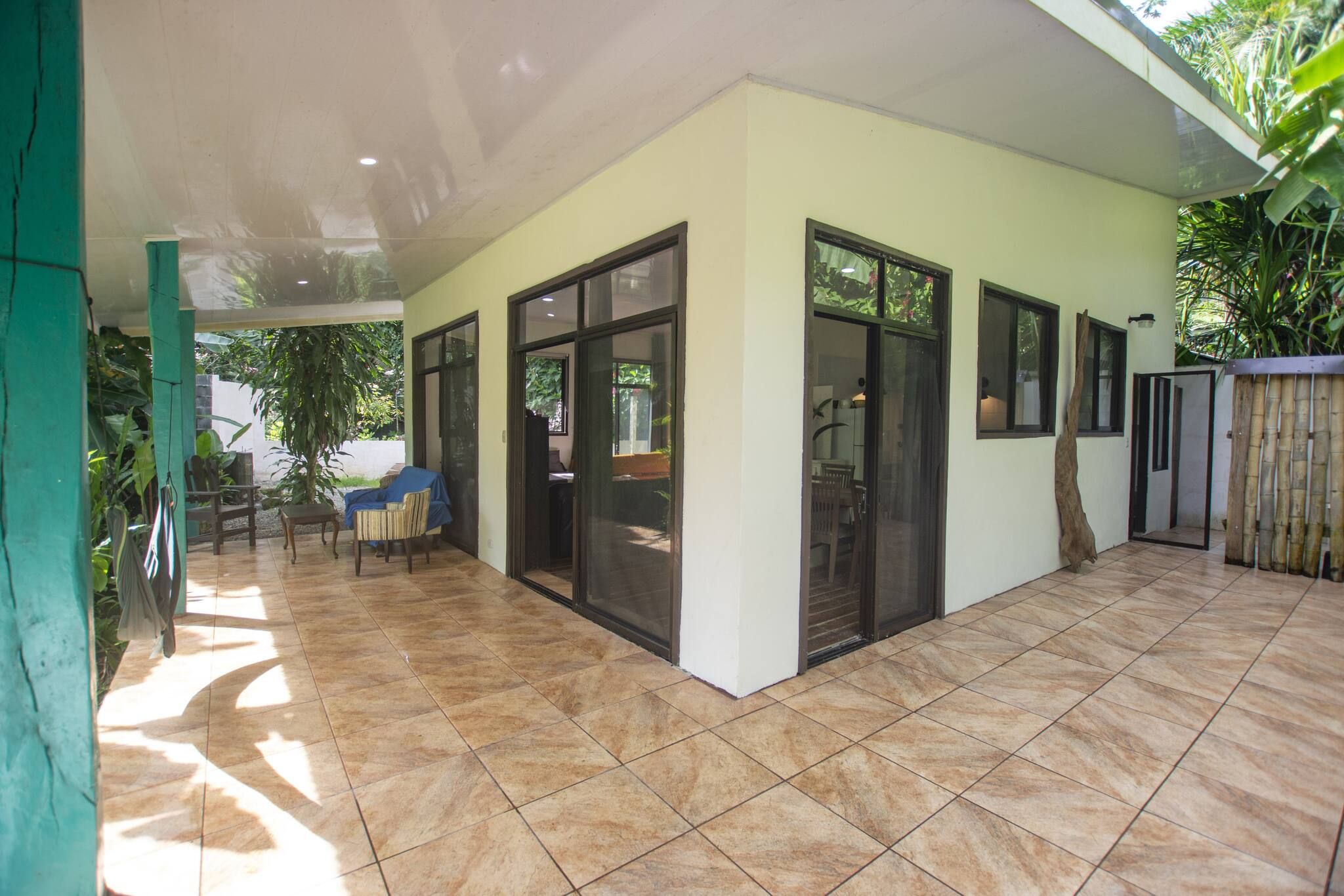Ein überdachter Patio-Bereich mit Fliesenboden, einer Sitzgruppe und einer Glastür zu einem Innenraum.