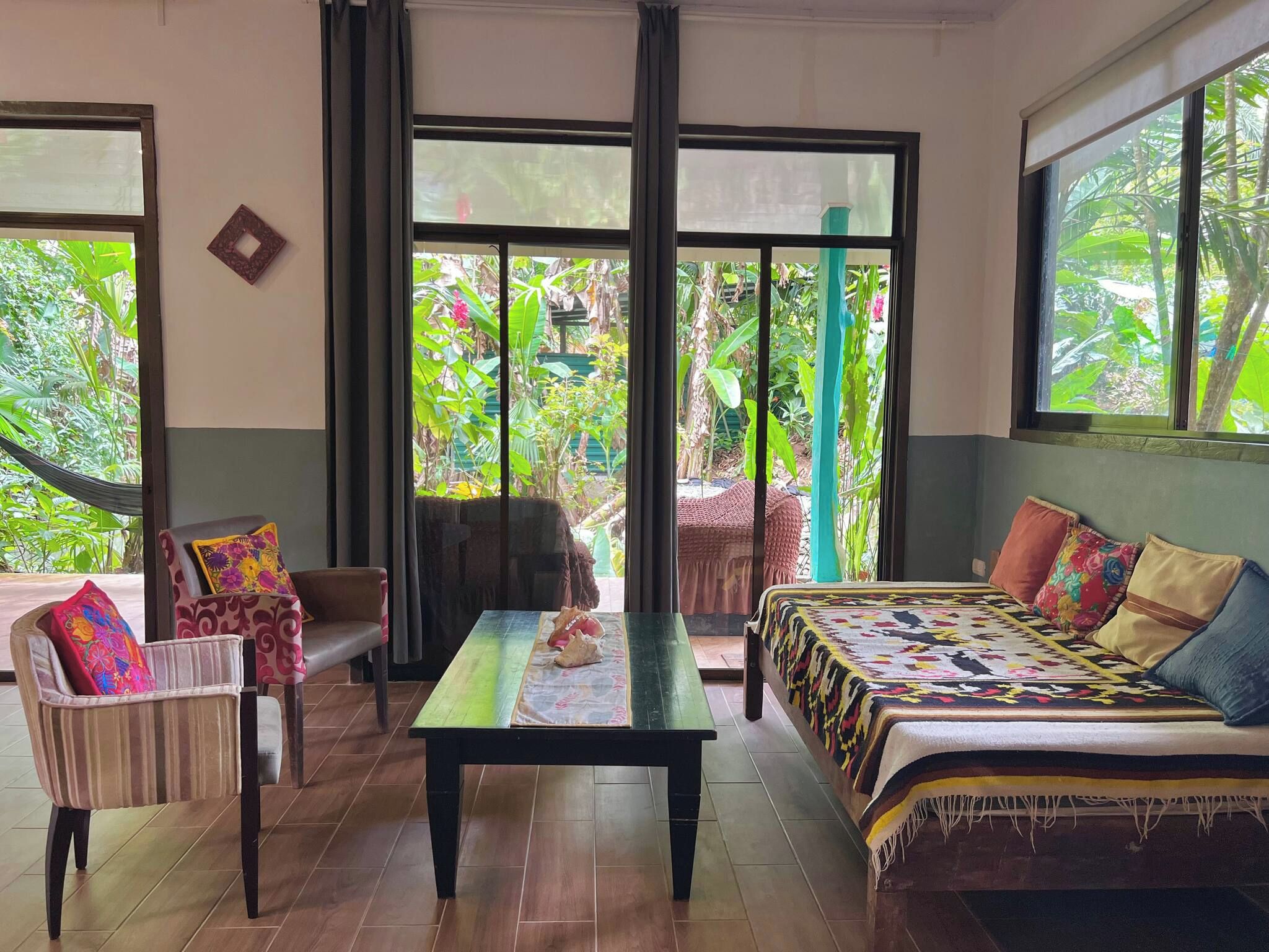 A room with a sofa, a chair, a table, and large windows with a view of greenery.