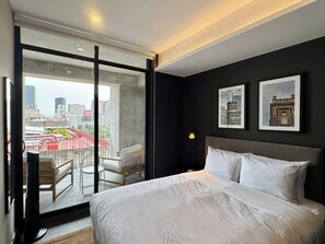 Ein modernes Hotelzimmer mit einem großen Bett, einem Balkon mit Blick auf die Stadt und zwei gerahmten Bildern an der Wand.