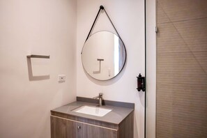 Et badeværelse med et rundt spejl, en vask og en håndklædestang.