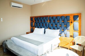 A hotel room with a large bed, a wooden headboard, a bedside table, a chair, and a small table with a chair. - w* | Deluxe 4BR in Prime Bocagrande (Cartagena de Indias)