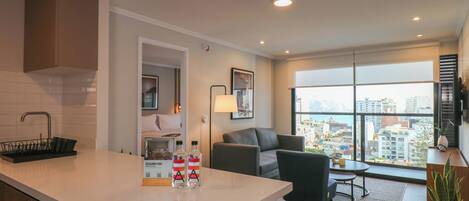 A modern kitchen with a white countertop, a black dish rack, and a view of the city through large windows.