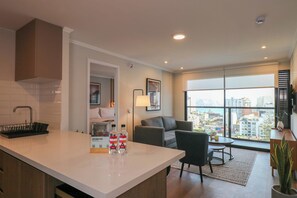 A modern kitchen with a white countertop, a black dish rack, and a view of the city through large windows. - w* | Chic 2BR w/ Balcony & Sea View in Miraflores (Miraflores)