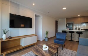 A modern living room with a TV, seating, a coffee table, and a kitchen area with bar stools. - w* | Chic 2BR w/ Balcony & Sea View in Miraflores (Miraflores)