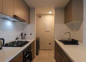 A compact kitchen with white tiles, stainless steel appliances, and wooden cabinets. - w* | Chic 2BR w/ Balcony & Sea View in Miraflores (Miraflores)
