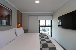 Een hotelkamer met een bed, een raam, een tv aan de muur en een schilderij.