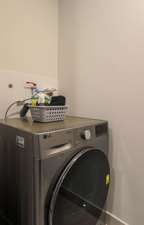 A compact, stainless steel LG ThinQ front-loading washing machine with a control panel and a basket of laundry on top. - w* | Chic 2BR w/ Balcony & Sea View in Miraflores (Miraflores)
