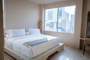 A modern bedroom with a large bed, a window with a city view, and a wicker chair. - w* | Upscale 3BR in Prime Bocagrande (Cartagena de Indias)