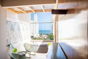 Ein Balkon mit Blick auf das Meer und Gebäude, ein Stuhl, ein kleiner Tisch und eine Pflanze.
