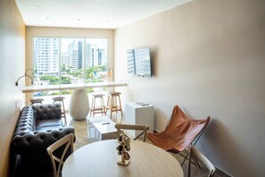 A modern living room with a sofa, chairs, a table, and a large window offering a city view. - w* | Signature 2BR w/ AC in Bocagrande (Cartagena de Indias)