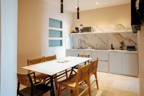 A modern kitchen with white cabinets, a marble backsplash, and a dining area with a white table and wicker chairs. - w* | Luxury 3BR in Prime Bocagrande (Cartagena de Indias)