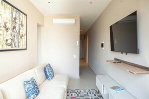 A modern living room with a white sofa, blue patterned pillows, a mounted TV, and a hallway leading to another room. - w* | Luxury 3BR in Prime Bocagrande (Cartagena de Indias)