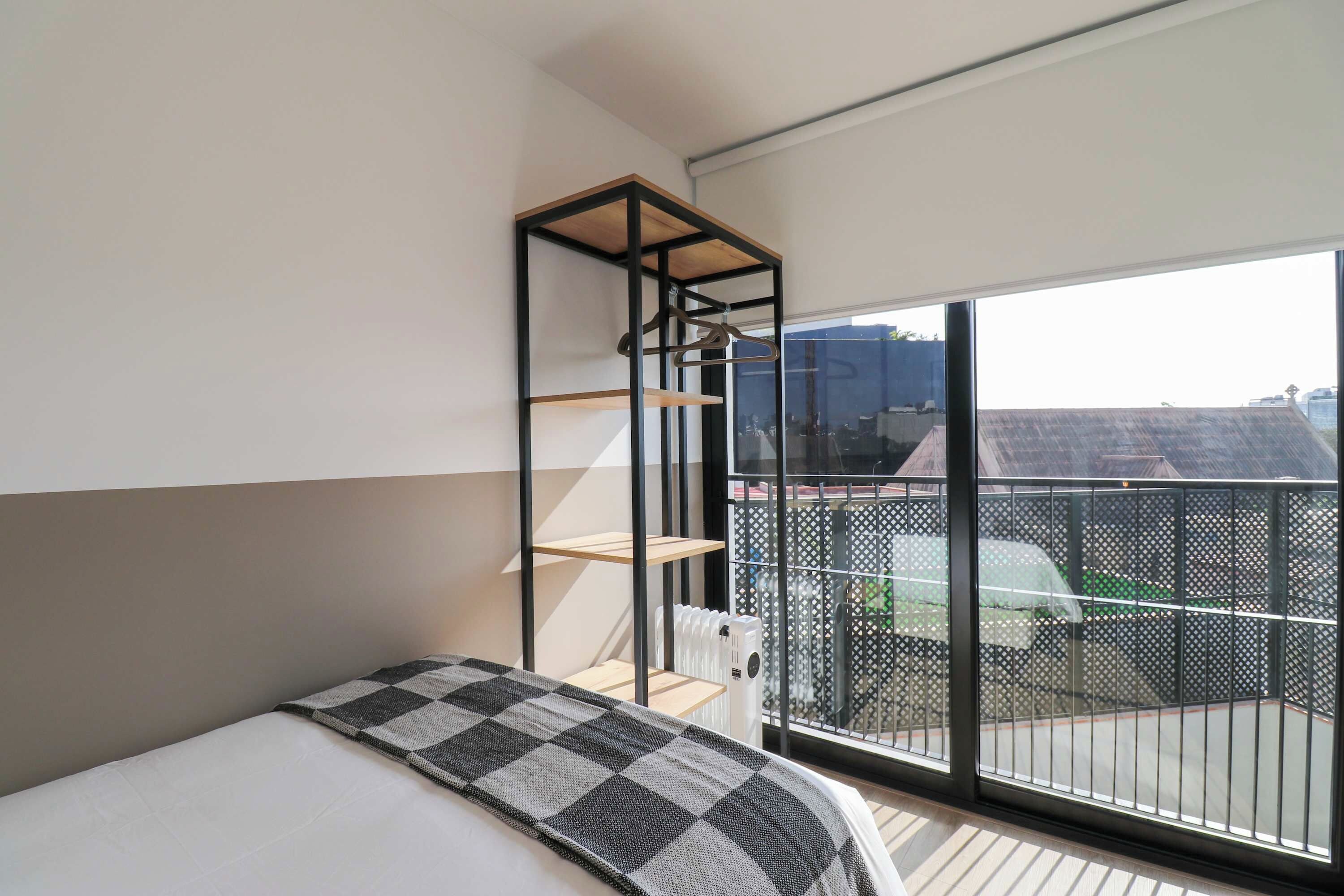 A bedroom with a bed, a hanging shelf, and a view of the outside.