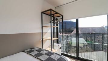 A bedroom with a bed, a hanging shelf, and a view of the outside.