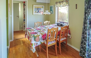 A dining area with a table covered in a floral tablecloth, wooden chairs, a hanging lamp, and a window with a view of greenery. - Cozy home in Visby with ethernet internet (Visby)