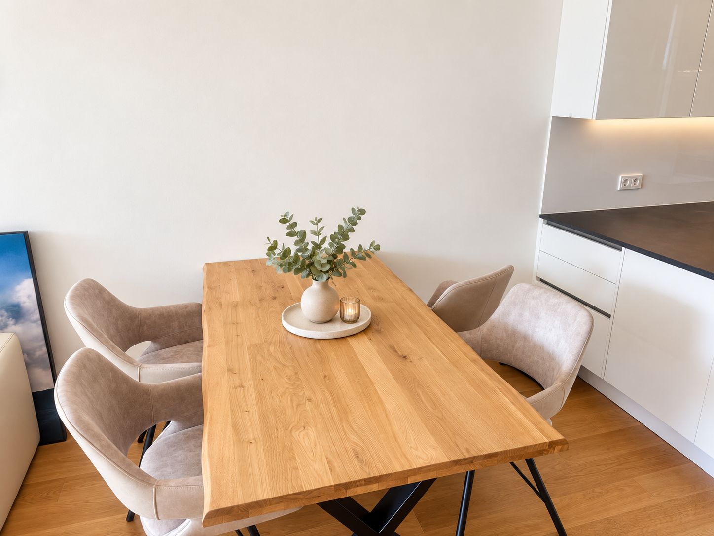 Un espace repas moderne avec une table en bois, deux chaises, un vase agrémenté de plantes et une cuisine en arrière-plan.