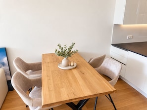 A modern dining area with a wooden table, two chairs, a vase with greenery, and a kitchen in the background. - Premium garden apartment on the Kreuzbergl near Lake Wörthersee, the University, and Lakeside (Klagenfurt am Wörthersee)