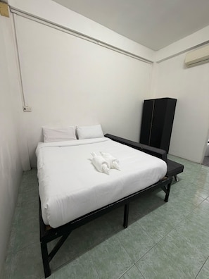 A single bed with a white mattress and pillows, a black headboard, a black wardrobe, and a tiled floor. - Global Sea View Hotel (Tambon Patong)