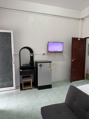 A room with a desk, a small refrigerator, a television mounted on the wall, and a door. - Global Sea View Hotel (Tambon Patong)
