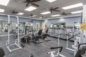 Un gimnasio con ventiladores de techo, equipo de ejercicio y una televisión.