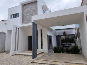 A modern two-story building with a flat roof, large windows, and a covered outdoor seating area. - Modern Rutelena Villa, sleeps 12, private pool, 5 min to 5th Street, the beach, and the supermarket (playa del carmen)