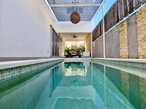 Ein Swimmingpool mit Deckenventilator, einer Liege und Blick ins Freie.