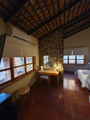 A room with a stone wall, a wooden desk, a chair, a bed, and a window with a view. - Sandy Shores 4B (La Paz)