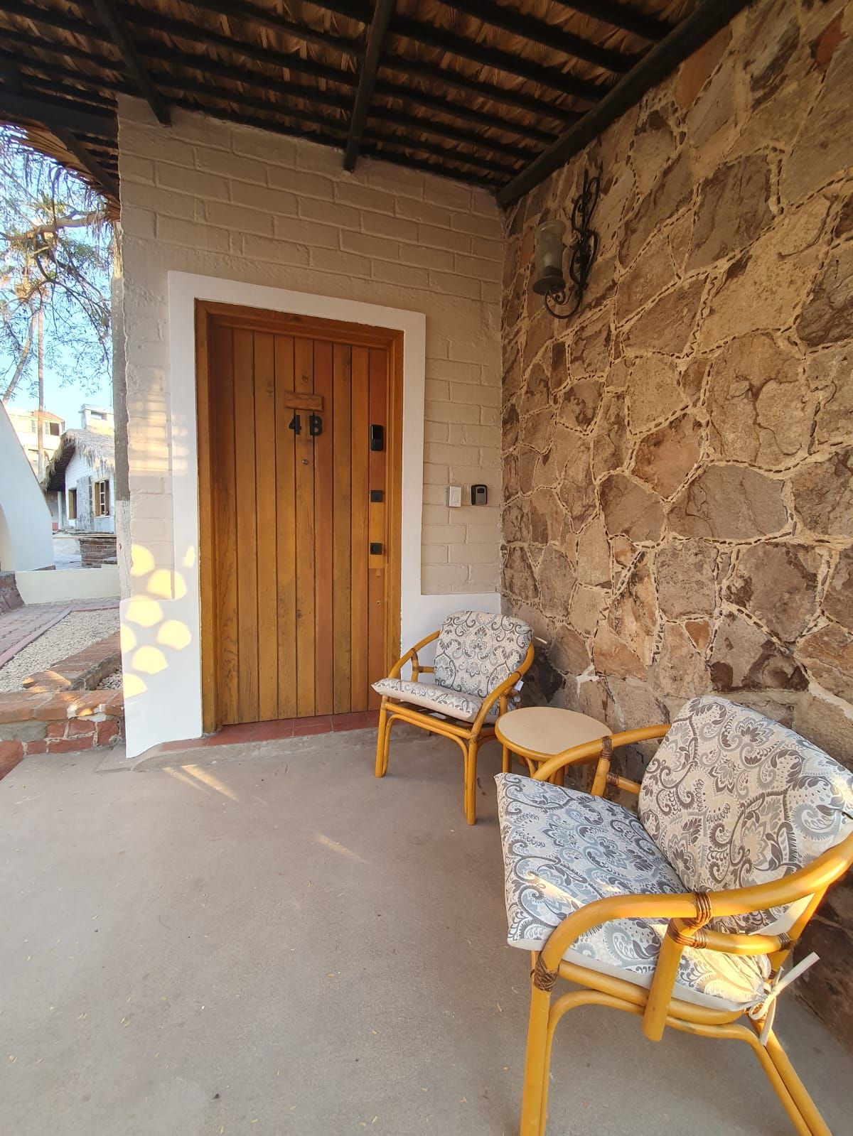A covered outdoor seating area with a stone wall, a wooden door, and a concrete floor.