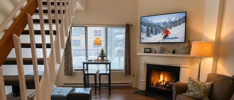 A living room with a fireplace, a television mounted on the wall, a ceiling fan, and a staircase.