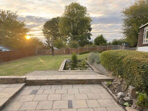 A backyard with a stone pathway leading to a pond, surrounded by a wooden fence and a large tree. - Modern 2-bed House With Garden Quiet Street, Easy London & Watford Access (Watford)