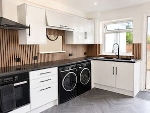 A modern kitchen with a built-in washer and dryer, white cabinetry, and a window providing a view of the outdoors. - Modern 2-bed House With Garden Quiet Street, Easy London & Watford Access (Watford)