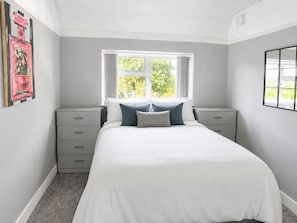 A bedroom with a bed, two bedside tables, a window, and a wall-mounted artwork. - Modern 2-bed House With Garden Quiet Street, Easy London & Watford Access (Watford)