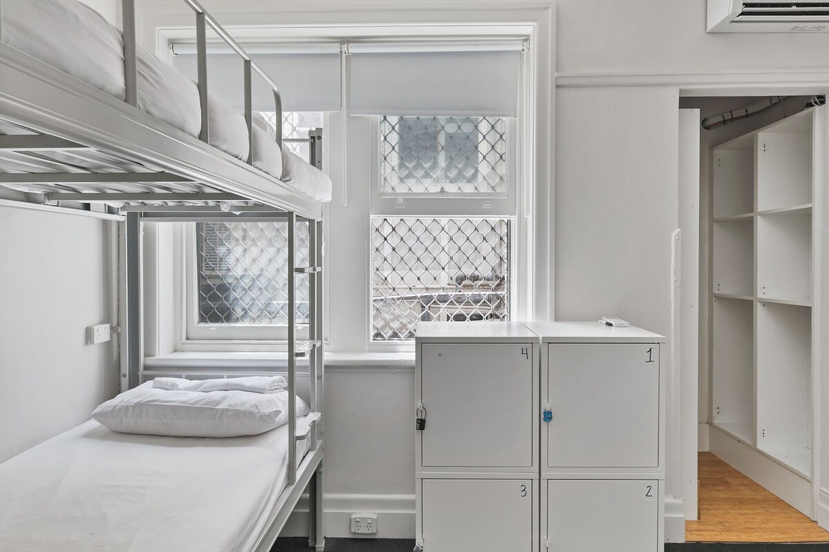Un dormitorio con literas, una ventana con rejas de metal, una pequeña cocina y un armario.