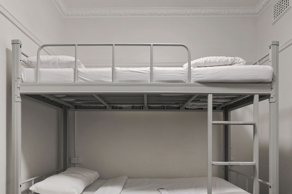 Una cama litera con ropa blanca y estructura metálica.