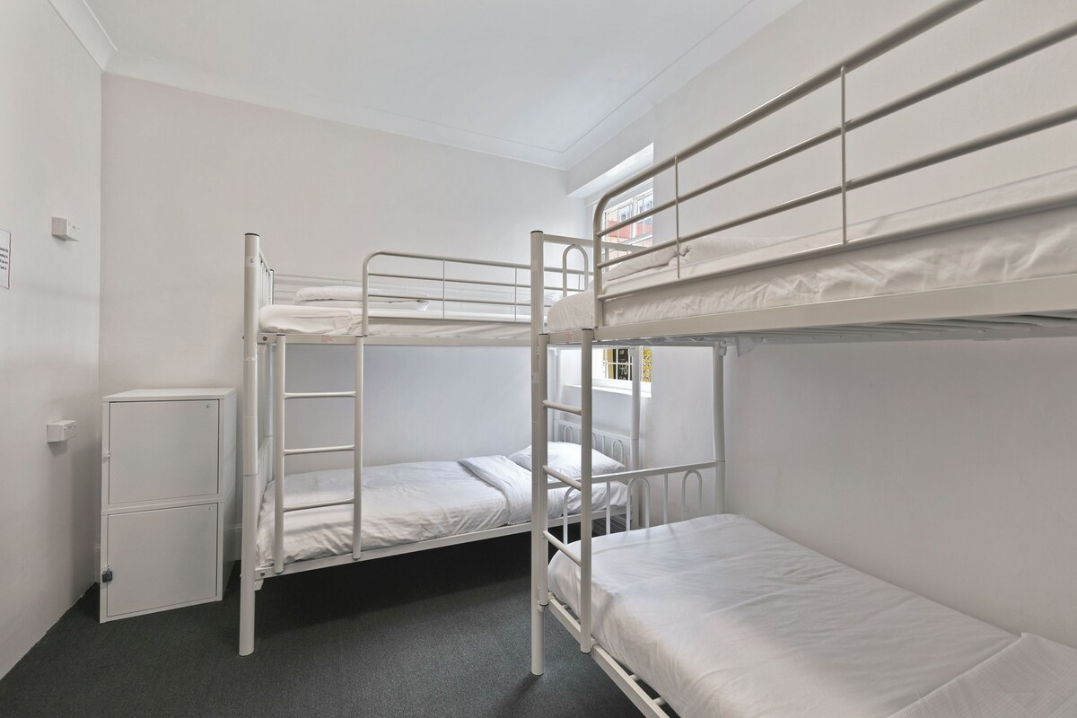 Un dormitorio tipo camarote con dos camas, un archivador pequeño y una ventana.