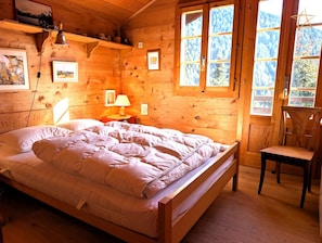 Habitació d'una cabana de fusta amb un llit, una tauleta de nit, una làmpada i una cadira.